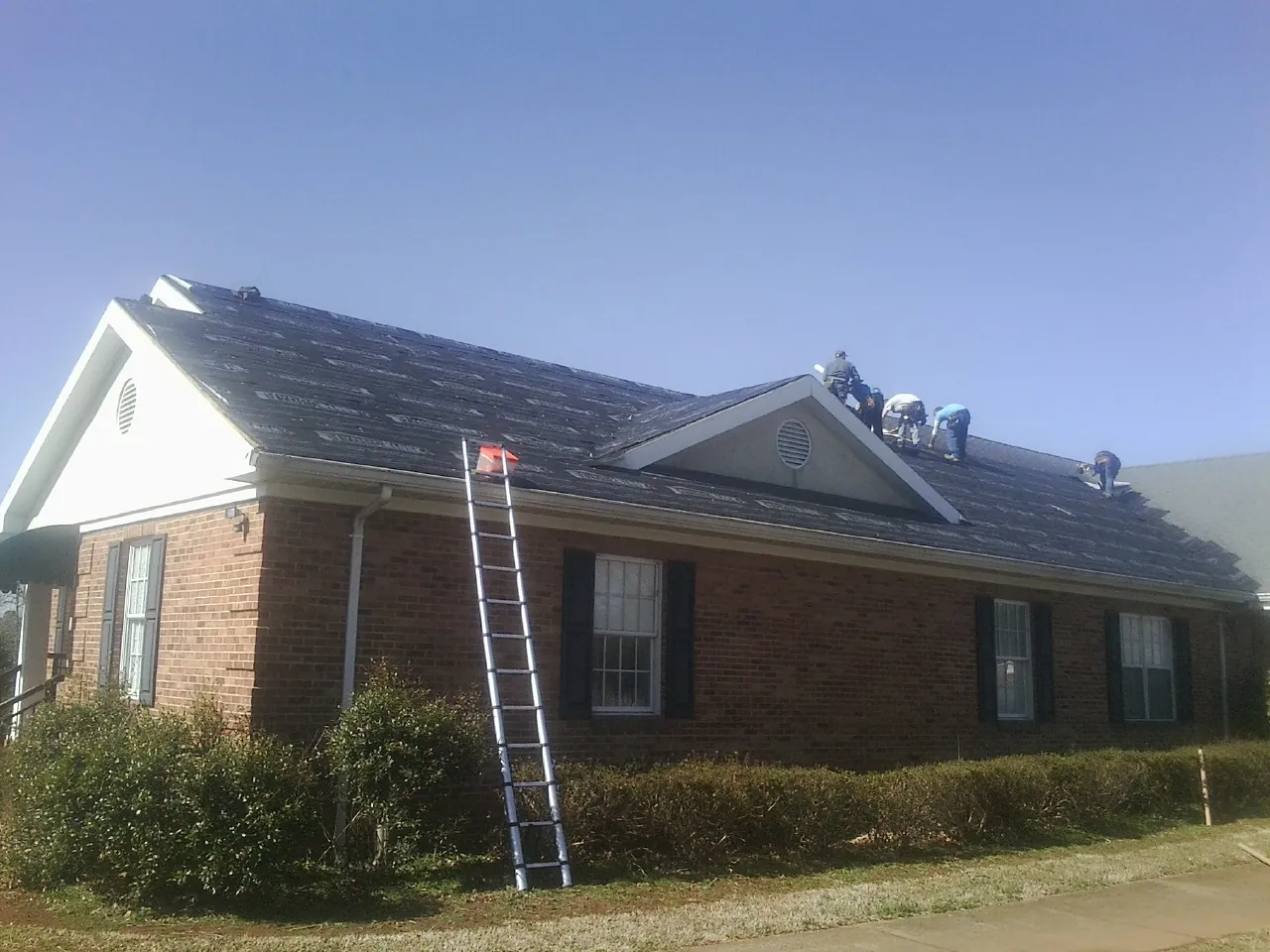 Crew tearing shingles off a brick ranch roof with a ladder set — Metal Roof Repair work by our crew in Schoharie