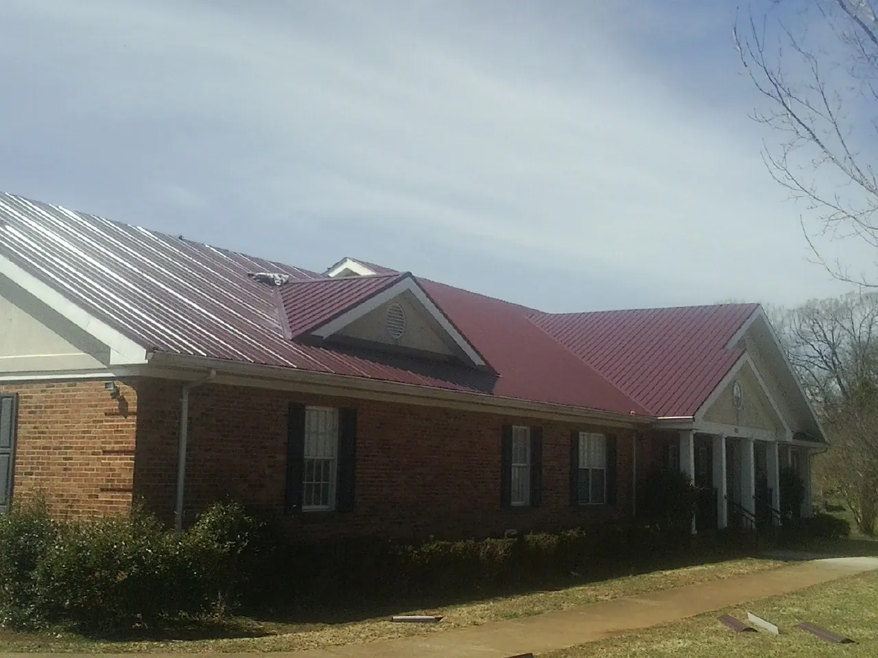 Red metal roof with gabled entries on a long brick building, from a Hail Damage Roof Repair job in Schoharie
