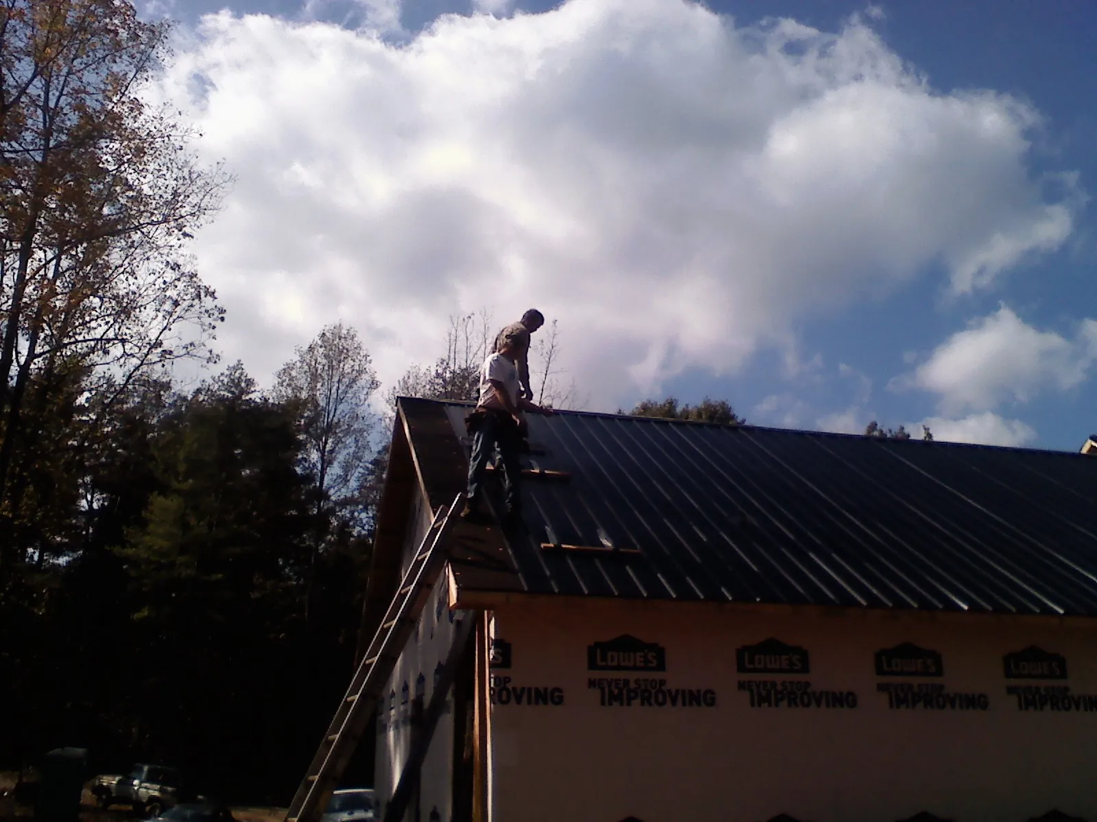Roofer fastening dark metal panels high against a cloudy sky, from a Roof Inspection job in Schoharie