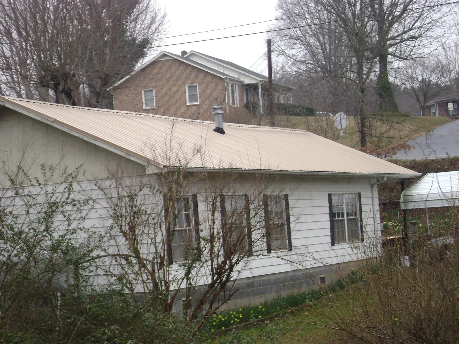 Tan metal roof on a white sided house set into a hillside — Commercial Roofing by Roofing Brothers in Schoharie