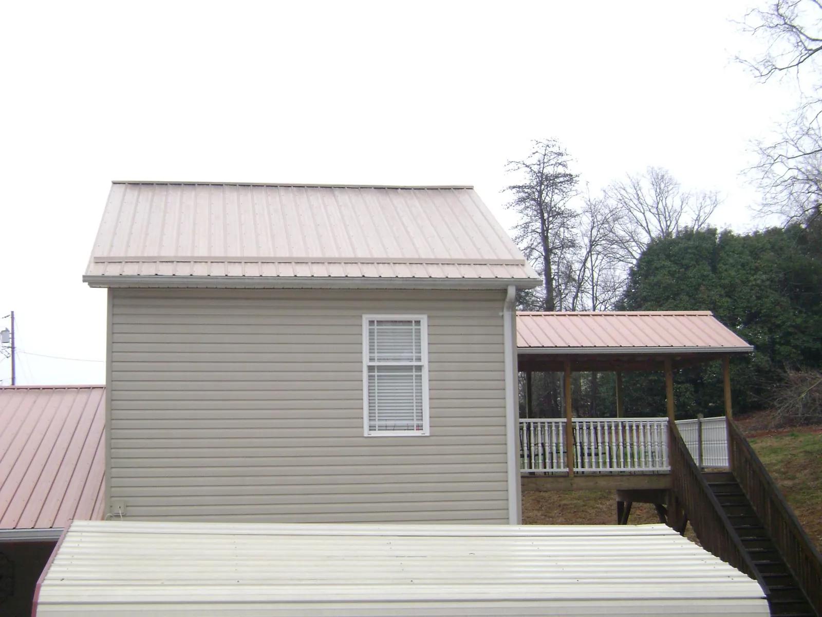 Tan metal roofs on a two story addition and attached porch, from a Roof Replacement job in Schoharie
